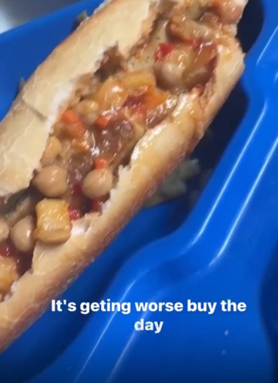 A baguette stuffed with chickpeas, peppers and brown stew in a blue prison meal tray